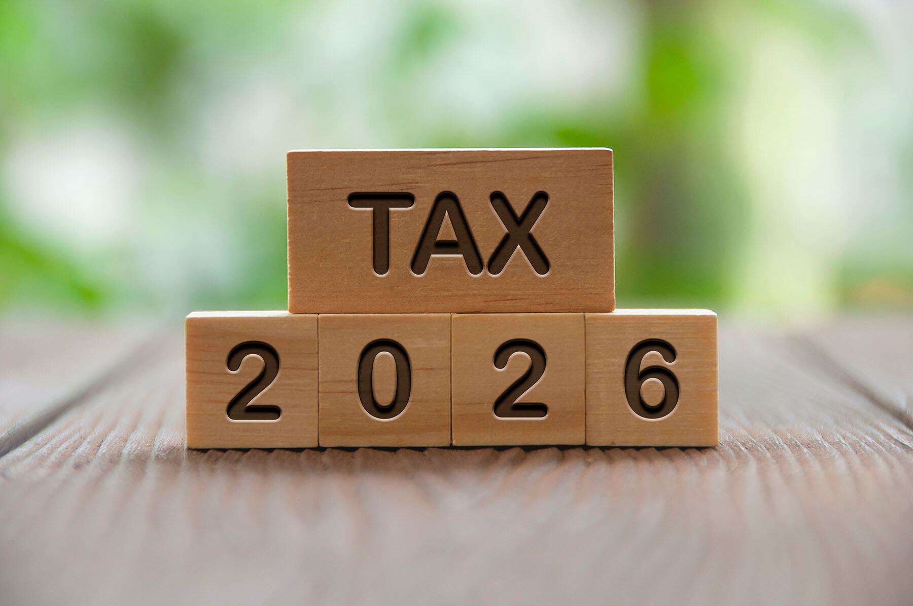 Wooden blocks displaying "TAX 2026" on a wooden surface with a blurred green background